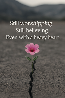 Pink flower sprouts from a cracked road; blurred mountains behind; text says still worshipping, still believing, with a heavy heart.